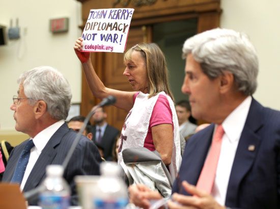 محتجة ترفع لافتة أثناء إدلاء وزير الخارجية الأميركي بشهادة جديدة بشأن سورية أمام الكونغرس