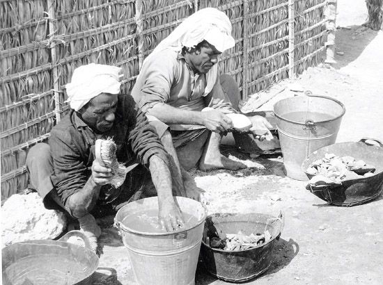 عاملان بحرينيان يقومان بغسل اللقيا من الخزف جوار معسكر القلعة