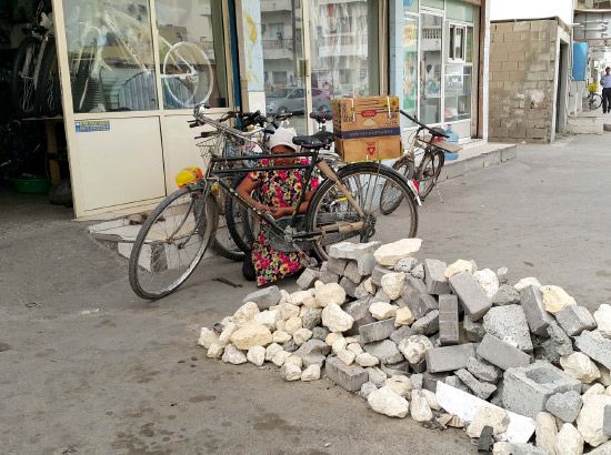 وحيدة تصلح إحدى الدراجات وأمامها الحجارة التي أغلقت شارع المحل
