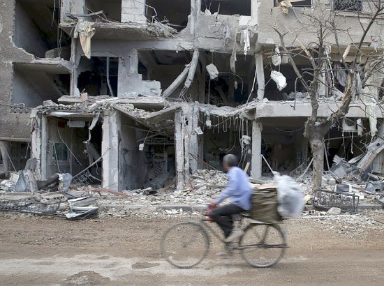 رجل على دراجته الهوائية يمر قبالة مبنى دُمِّر في إحدى ضواحي دمشق بفعل الصراع في سورية - reuters