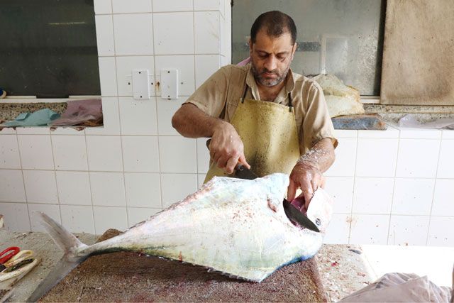 أحد العاملين خلال توليه تنظيف وتقطيع سمكة كبيرة الحجم في سوق المنامة المركزي - تصوير :محمد المخرق