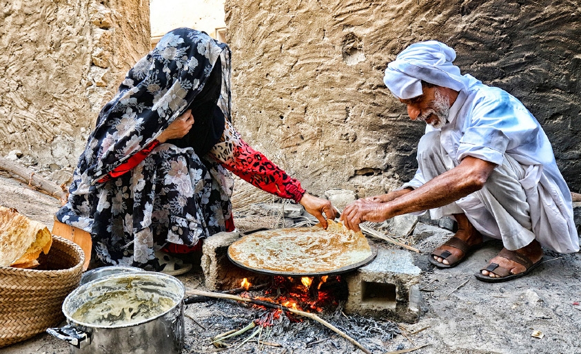 ﻿أم محمد مع والدها يُعدّان خبز التاوه ويضعانه في «سلة الحصير»
