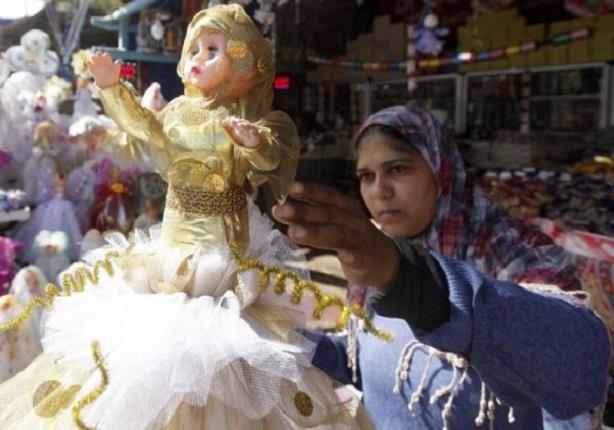 سيدة مصرية تقف بالقرب عروسة المولد الشعبية 