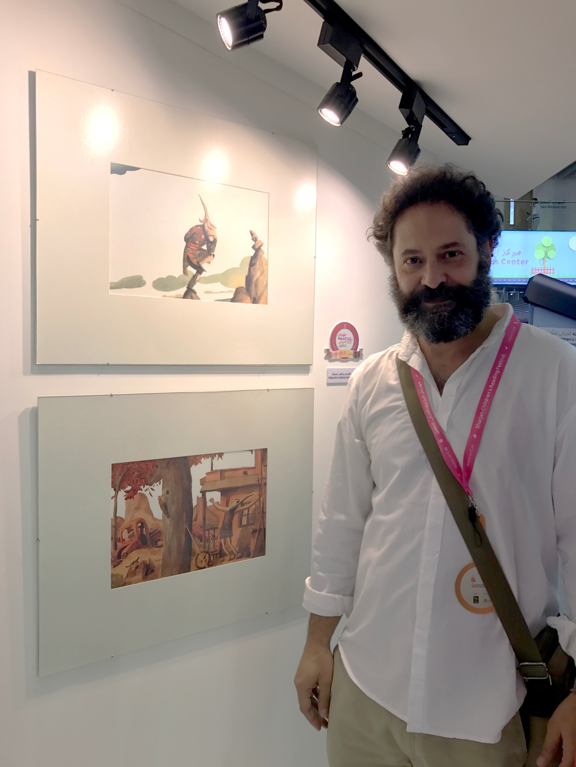 الاسباني أليخاندرو غاليندو بيدراغو بجانب لوحاته الفائزة بالمركز الأول في معرض الشارقة لرسوم كتب الطفل 2017  