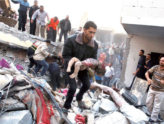 فلسطينيون يحملون جثة طفل من تحت أنقاض منزل هدمته غارة إسرائيلية بغزة - رويترز