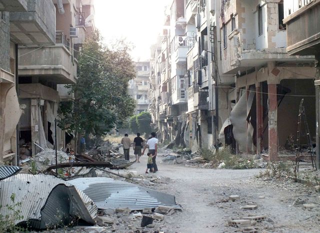 أشخاص يمشون وسط المباني المدمرة في حمص - REUETRS
