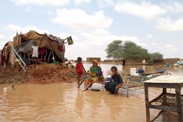 عائلة سودانية تجلس بجانب منزلها في شارع غمرته المياه في ضواحي الخرطوم - AFP